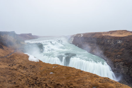 The majestic Gullfoss waterfall in Iceland, formed by the Hvita river cascading down two tiers into a narrow canyon. The powerful water flow and misty spray create a breathtaking sight.の写真素材