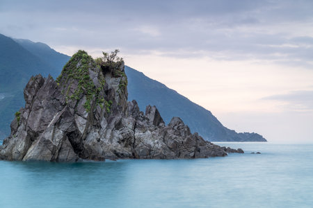 At dusk. Gentle waves lap against smooth, rounded rocks in a tranquil cove. The sky is painted in soft hues of pink and purple, reflecting on the calm water. Suao, Yilan, Taiwan.の写真素材