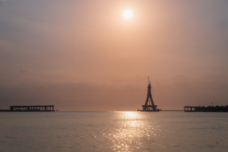 A majestic silhouette of the Tamsui Bridge under construction is bathed in the golden hues of sunset. The unfinished structure stands tall against a vibrant sky. Tamsui, Taiwan.の写真素材