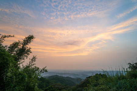 A peaceful evening scene with a soft, pastel sky. The clouds are gently drifting across the horizon, casting a warm glow over the landscape. Captured at sunset in Dading Mountain, Shulin, Taiwan.の写真素材