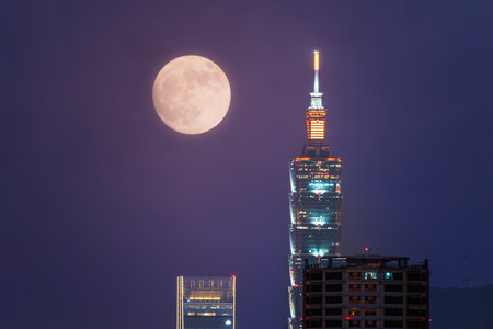 A golden autumn moon hangs over the Taipei skyline, casting a warm glow on the city. The scene captures the tranquility of an autumn evening. Taipei City, Taiwan.の写真素材
