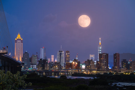 A golden autumn moon hangs over the Taipei skyline, casting a warm glow on the city. The scene captures the tranquility of an autumn evening. Taipei City, Taiwan.の写真素材