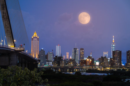A golden autumn moon hangs over the Taipei skyline, casting a warm glow on the city. The scene captures the tranquility of an autumn evening. Taipei City, Taiwan.の写真素材