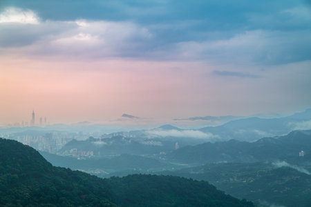 A breathtaking view of a valley shrouded in mist, with distant mountains peeking through the clouds. The lush greenery and soft, natural light create a beautiful and calming scene.の写真素材