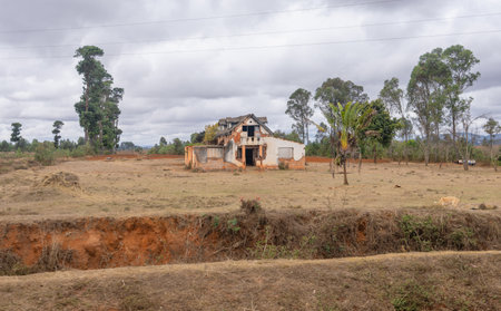 An abandoned red brick house stands alone in the middle of a field. The road leading to the park is lined with this rustic scenery. Isalo National Park, Madagascar.の写真素材