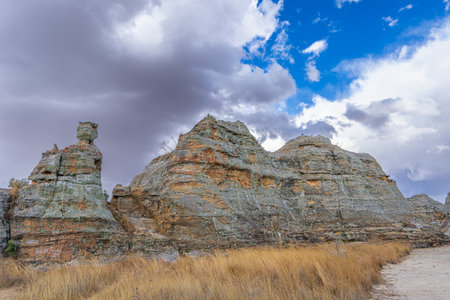 Iconic Queen of Isalo sandstone rock formation with distinctive crown-like top under dramatic cloudy sky. Natural weathered limestone cliffs surrounded by grass. Isalo National Park, Madagascar.の写真素材
