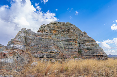 Iconic Queen of Isalo sandstone rock formation with distinctive crown-like top under dramatic cloudy sky. Natural weathered limestone cliffs surrounded by grass. Isalo National Park, Madagascar.の写真素材