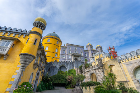 The vibrant yellow and grey Pena Palace stands majestically under a clear blue sky. The unique architecture and lush surroundings make it a captivating sight. Sintra, Portugal.の写真素材