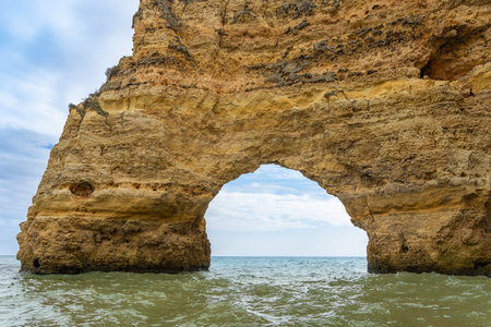 Stunning coastal cliffs with intricate sea caves, showcasing layers of golden and reddish rock formations. The turquoise waters add to the breathtaking scenery. Algarve, Portugal.の写真素材