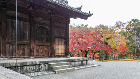 A traditional wooden temple building at Nanzen-ji with vibrant autumn foliage in the background. A serene and historic scene in Kyoto. Nanzen-ji Temple, Kyoto, Japan.の写真素材