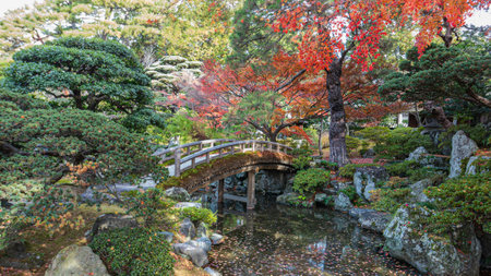 A tranquil scene of a wooden bridge over the Onnai Pond at Kyoto Imperial Palace, surrounded by lush greenery and autumn colors. A peaceful oasis. Kyoto, Japan.の写真素材