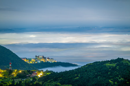A university stands illuminated atop Datun Mountain, Taipei, Taiwan, surrounded by mist and clouds on a spring night. The serene and mystical atmosphere is captured beautifully in this image.の写真素材