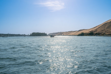 A picturesque view of the Nile River flowing near the Aswan High Dam in Egypt on a bright spring day. The sun glints on the water amidst the tranquil landscape.の写真素材