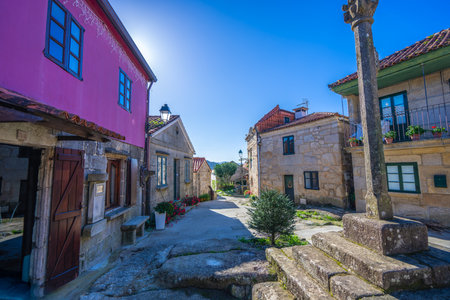 A sunny street in Combarro, Spain, showcasing traditional Galician stone houses and a carved cross...