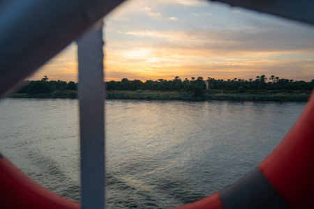 A captivating sunset over the Nile River near Esna Lock, Aswan, Egypt, viewed from a cruise ship. The sky displays soft colors above the peaceful water and lush green banks.の写真素材