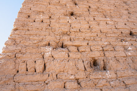 Close-up of an ancient mud brick wall at Abu Simbel, Aswan, Egypt, showing weathering and small holes, likely sparrow nests. This texture offers a glimpse into historical construction.の写真素材
