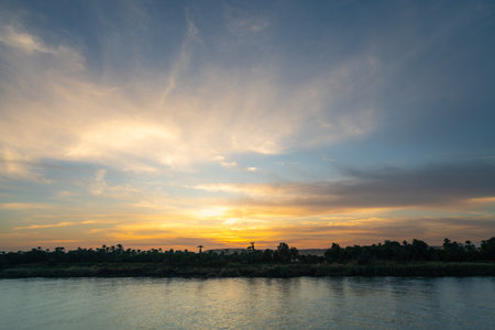 A tranquil cruise boat glides at sunset near Esna Lock on the Nile River, Egypt, capturing golden serenity.の写真素材