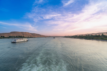 A tranquil scene on the Nile River near Esna Lock in Aswan, Egypt, as two cruise boats navigate the waters during a beautiful dusk with soft, colorful skies and distant desert banks.の写真素材