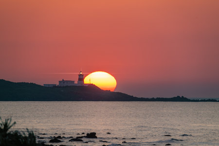 Vibrant sunset over the Shimen coastline in New Taipei City Taiwan, featuring the iconic Fuguijiao Lighthouse and coastal rock formations.の写真素材