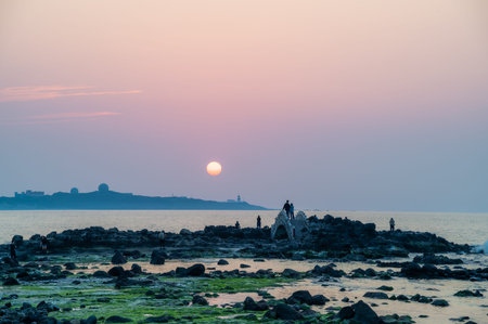 Visitors line up to capture the spring sunset behind Fugui Cape Lighthouse as golden rays illuminate the coastal landscape. Shimen, Taiwan.の写真素材