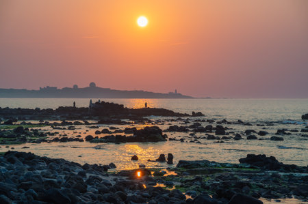 A breathtaking sunset illuminates the Fuguijiao Lighthouse coastline in Shimen, New Taipei City, Taiwan, as visitors gather to witness the stunning natural spectacle.の写真素材