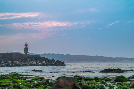 Golden sunset light reflects on the calm harbor waters at Fugui Cape during spring, with silhouettes of boats and breakwater structures framing the tranquil view. Shimen, Taiwan.の写真素材