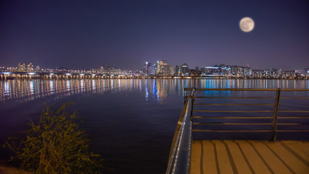 A full moon is reflected on the Han River at night in Yeouido, Seoul, South Korea. The city landscape is set against the bright lights, creating a stunning visual effect.の写真素材