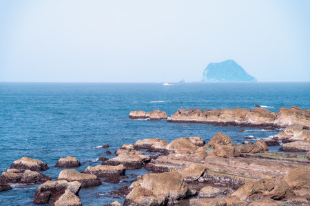 The rugged rocky coastline in Shimen District New Taipei City Taiwan with the distinctive silhouette of Keelung Islet in the distance on a clear afternoon.の写真素材
