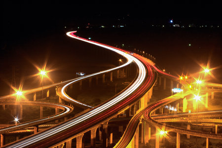 A spectacular long exposure shot of the Zhongqing Interchange in Taichung, Taiwan, at night, featuring a complex road network and stunning light trails from vehicles.の写真素材