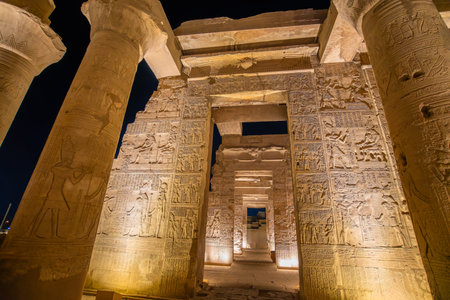 Night illumination reveals detailed hieroglyphic carvings on massive stone columns inside the ancient Temple of Kom Ombo in Egypt.の写真素材