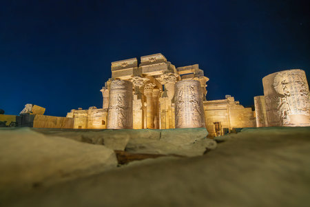 A night time view of the illuminated wall and ancient hieroglyphs of the Temple of Kom Ombo. The historic site shines brightly against a dark sky.の写真素材