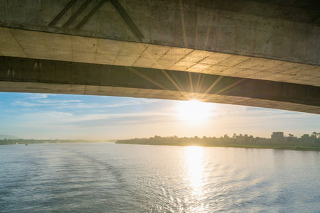 A serene sunset view on the Nile River, captured from a cruise ship. The sun's rays shine under a...