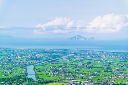 A breathtaking high-angle view of the Lanyang Plain in Dongshan, Yilan County, Taiwan, with the majestic Guishan Island visible in the distance across the blue sea, under a sky with serene clouds.の写真素材