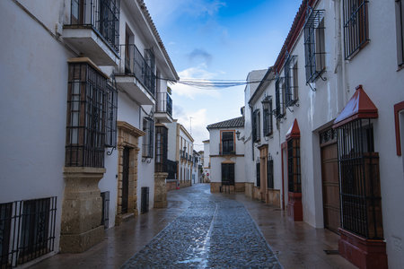 Ronda, Spain - A quiet cobblestone street glistens after spring rain. Whitewashed buildings and...