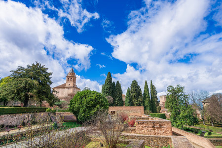 A scenic view of the lush gardens with cypress trees and the bell tower of the Church of Santa Maria at the historic Alhambra in Granada, Spain.の写真素材