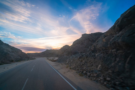Stunning sunset highway view with rugged hills, power lines, and dreamy clouds, captured in spring...