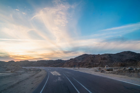 Road view of the desert highway winding through rocky mountains at dramatic twilight on the approach...