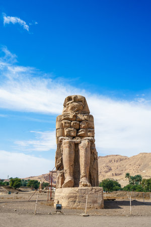 A massive stone statue of Pharaoh Amenhotep III at Colossi of Memnon archaeological site in Luxor, Egypt under clear blue sky.の写真素材