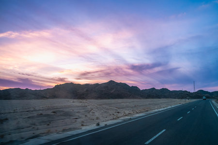 Truck driving on highway to Hurghada, Egypt, with rugged hills, power lines, and dreamy clouds, captured in spring 2025 during a journey.の写真素材