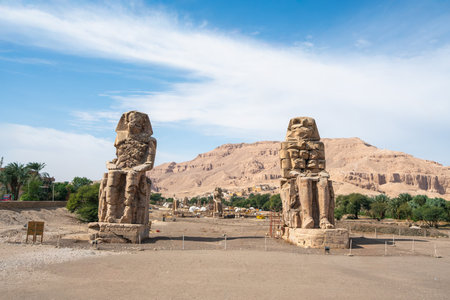 The Colossi of Memnon two massive stone statues of Pharaoh Amenhotep III stand in the desert landscape of Luxor Egypt backed by the Theban Hills.の写真素材