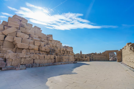 Expansive courtyard with massive sandstone walls at Temple of Karnak in Luxor, Egypt. Ancient Egyptian architecture under blue sky with clouds.の写真素材