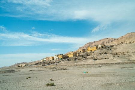 A remote hillside settlement near Clossi of Memnon in Luxor Egypt, featuring yellow buildings, rocky terrain, desert vegetation, and clear skies.の写真素材