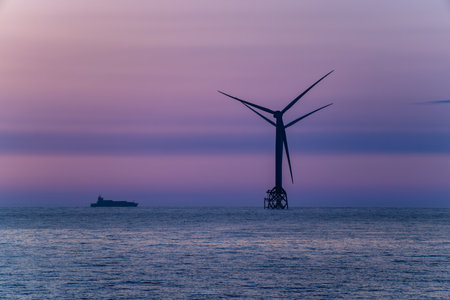A spectacular twilight view of a stationary wind turbine and a freighter in the sea, set against the beautiful, calm, and colorful sky over Miaoli, Taiwan.の写真素材