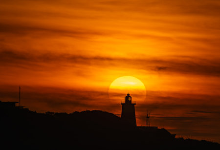 A majestic sunset video at Fuguei Cape Lighthouse in Shimen New Taipei City Taiwan. The sun sinks behind the landmark lighthouse creating a stunning silhouette against an orange sky.の写真素材