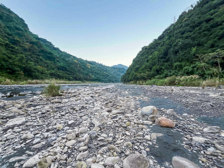 Morning view of Wulai river gorge in New Taipei City, Taiwan. Clear stream flows through rocky riverbed surrounded by lush green mountain slopes.の写真素材