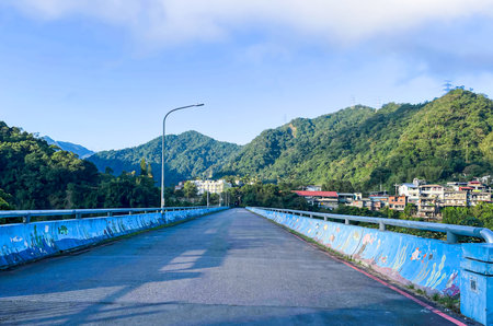 Empty bridge with vibrant blue ocean mural on barriers leading to mountain village in Wulai, New Taipei City, Taiwan. Early morning light and lush green hills.の写真素材