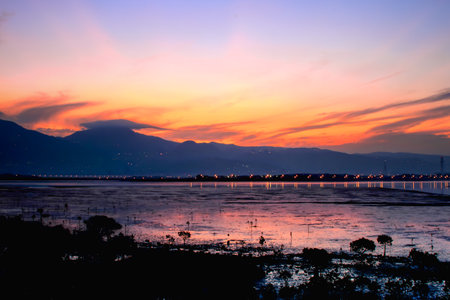 Beautiful sunrise at Wugu Wetland in New Taipei City, Taiwan. Orange and purple sky reflects on wetland water with mountain silhouettes and lights.の写真素材
