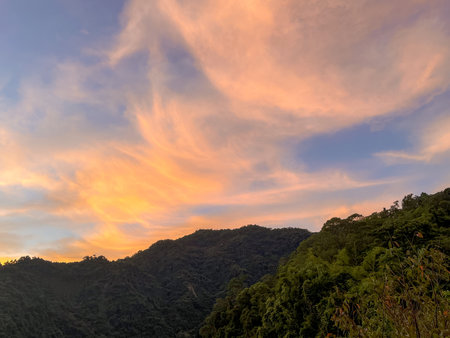 Spectacular sunrise sky with wispy pink and orange clouds above the dense, dark green mountain range in Wulai, New Taipei City, Taiwan, highlighting natural beauty.の写真素材
