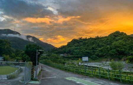 Vibrant sunrise with fiery orange clouds above the misty green mountains of Wulai, New Taipei City,...