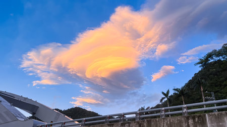 Rare golden lenticular cloud glowing at sunrise above Wulai mountains in New Taipei City Taiwan with bridge foreground.の写真素材